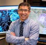 Photo of Sam Ng in front of two monitors displaying weather maps