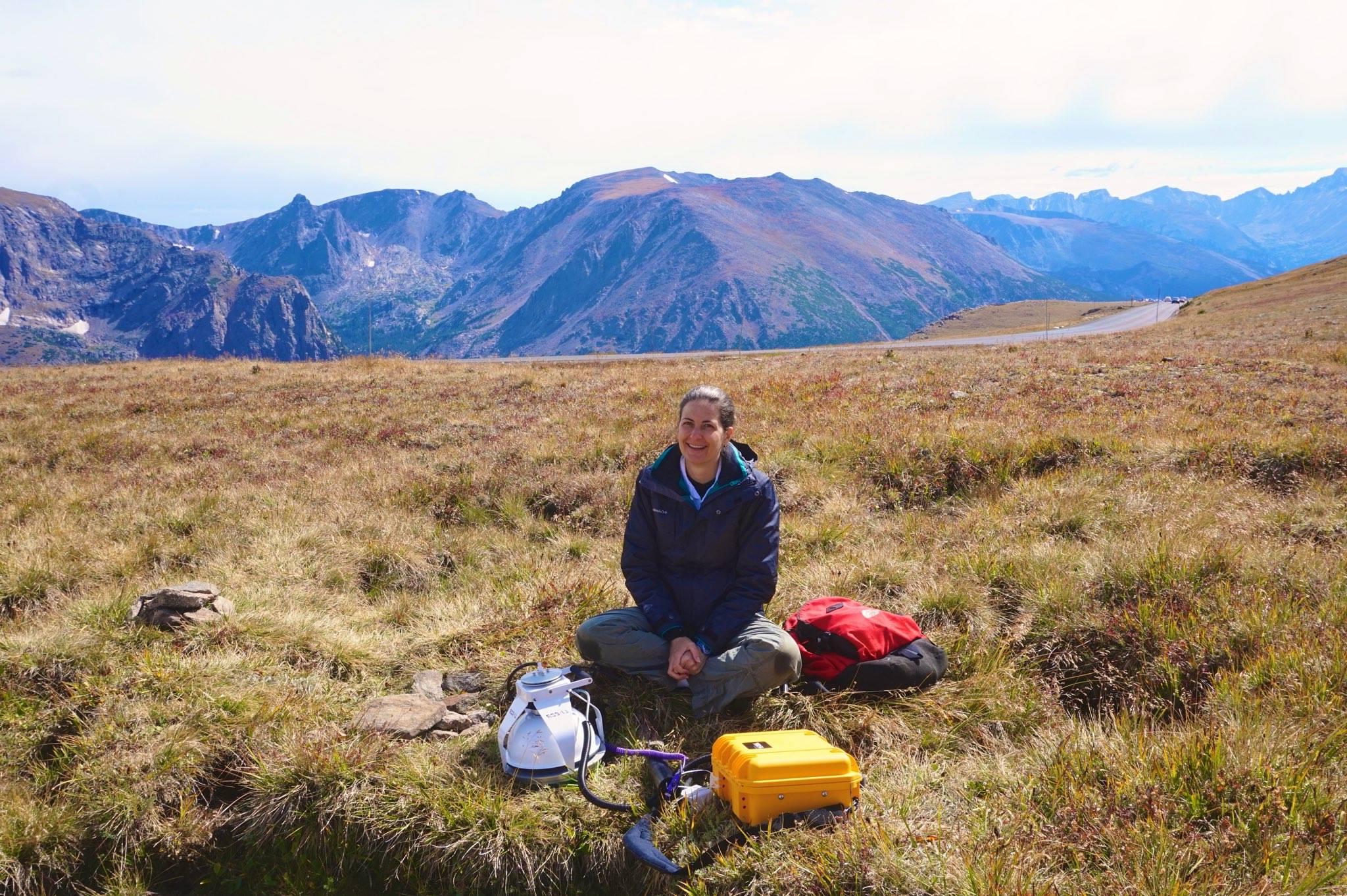 Professor Sarah Schliemann sitting in a high elevation field with mountains behind her.