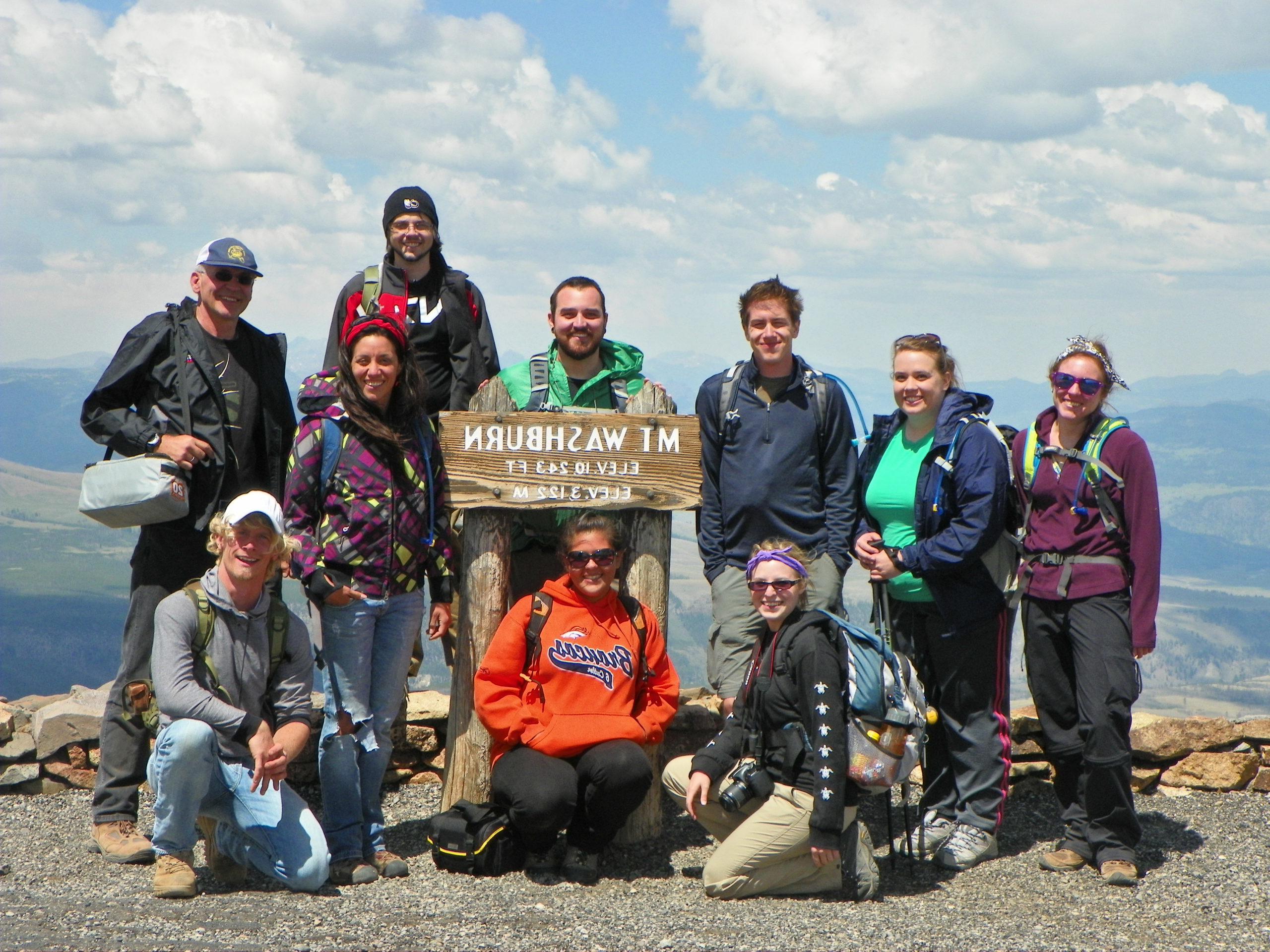 ten hikers posing with Mt. Washburn summit sign