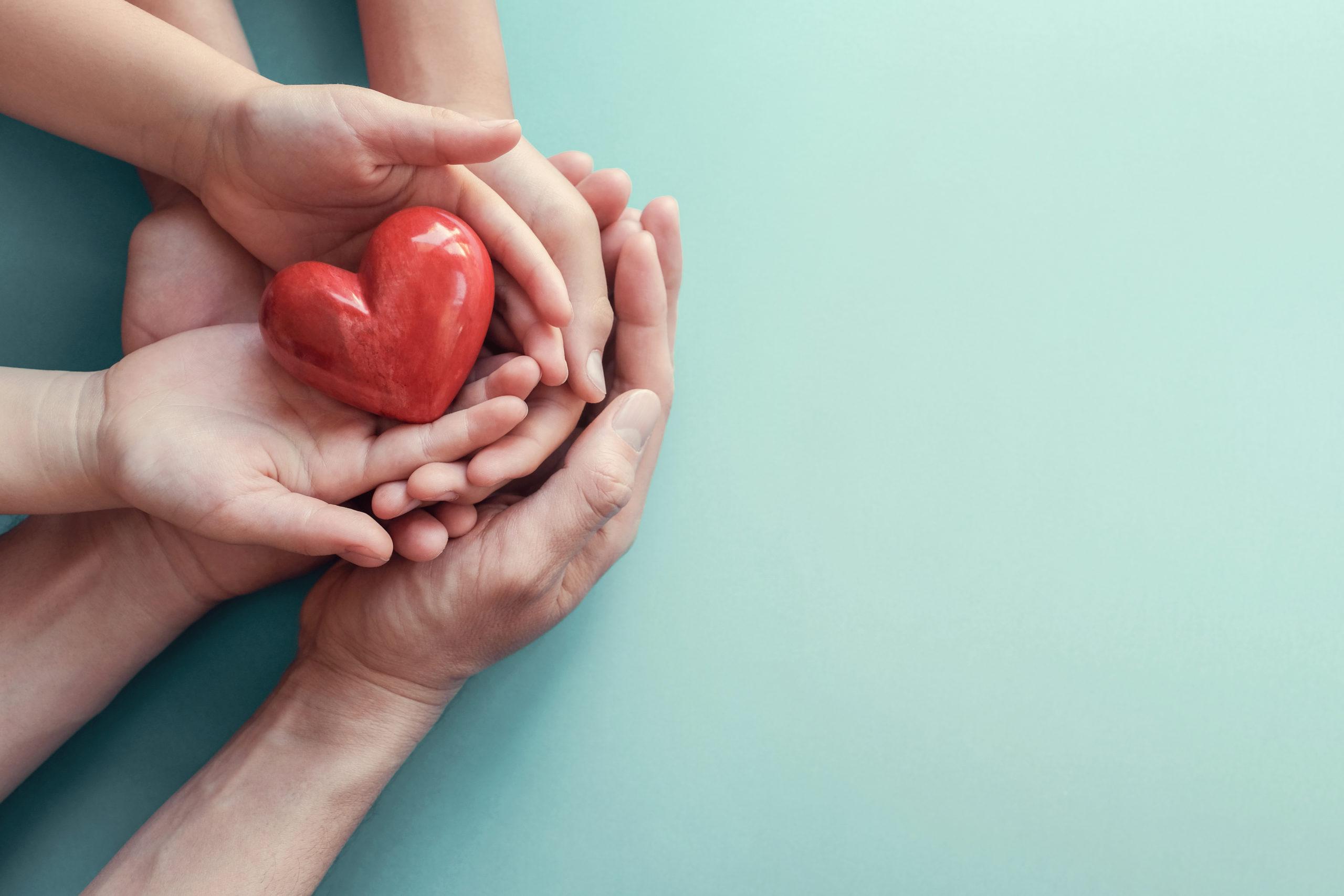 Adult and child hands holding red heart on aqua background