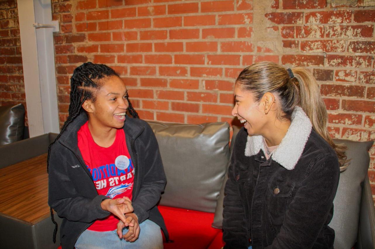 Two students in front of brick wall laughing