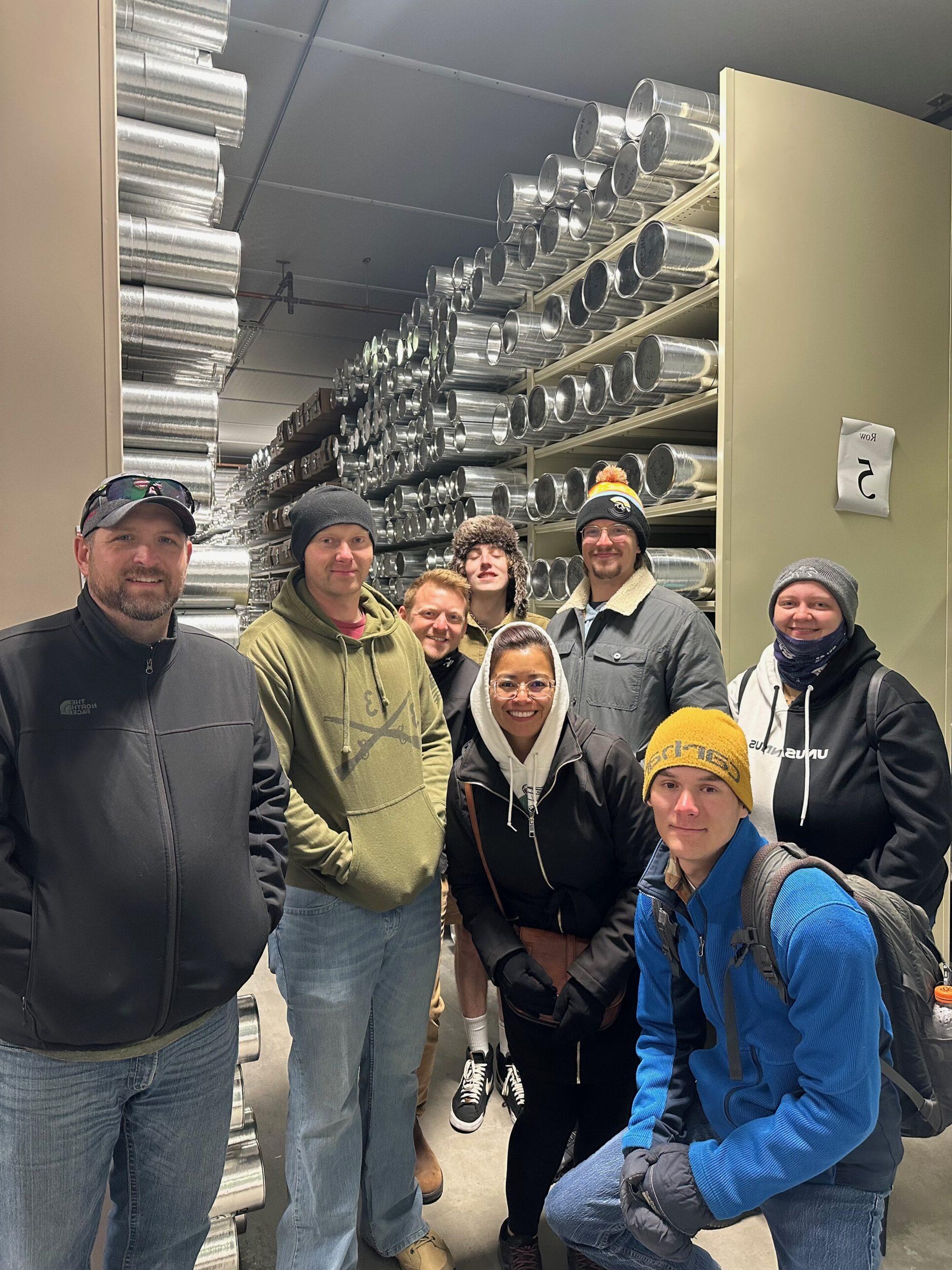 Students pose for a photo in front of several metal tubes containing ice cores at the ice core laboratory