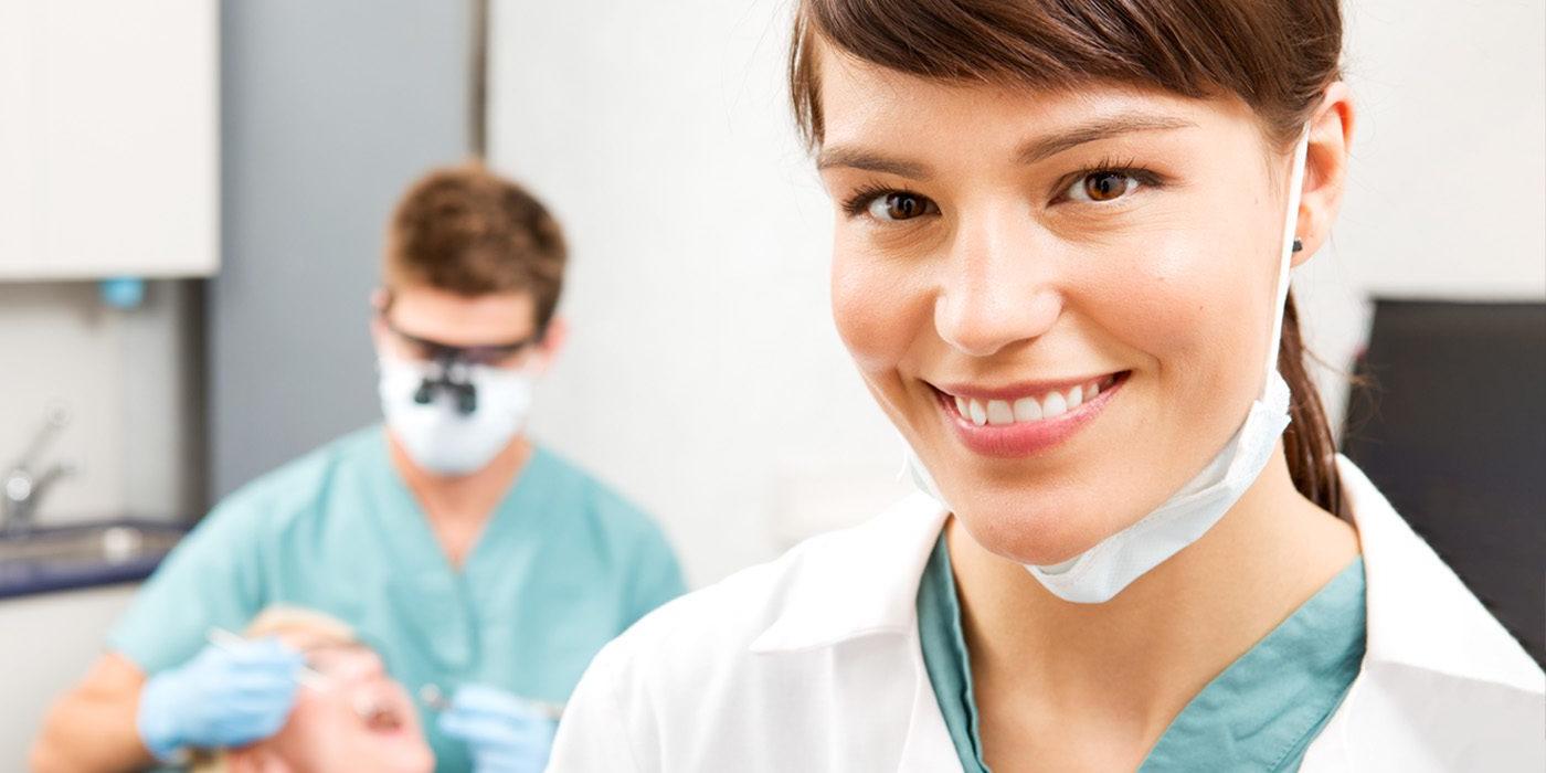 Smiling Dental assistant with dentist working with patient in background