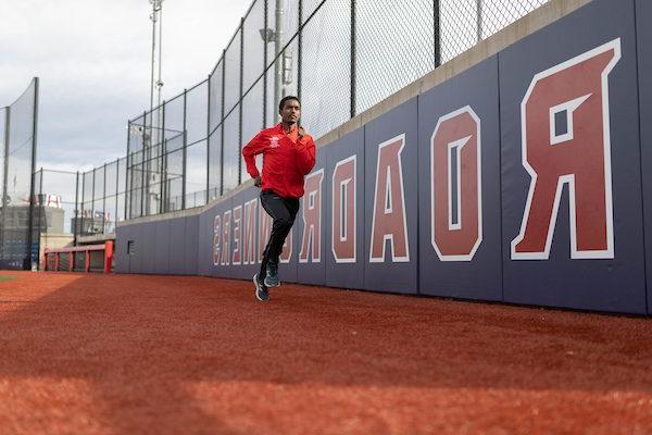 A man in a red MSU Denver zip-up runs around the track